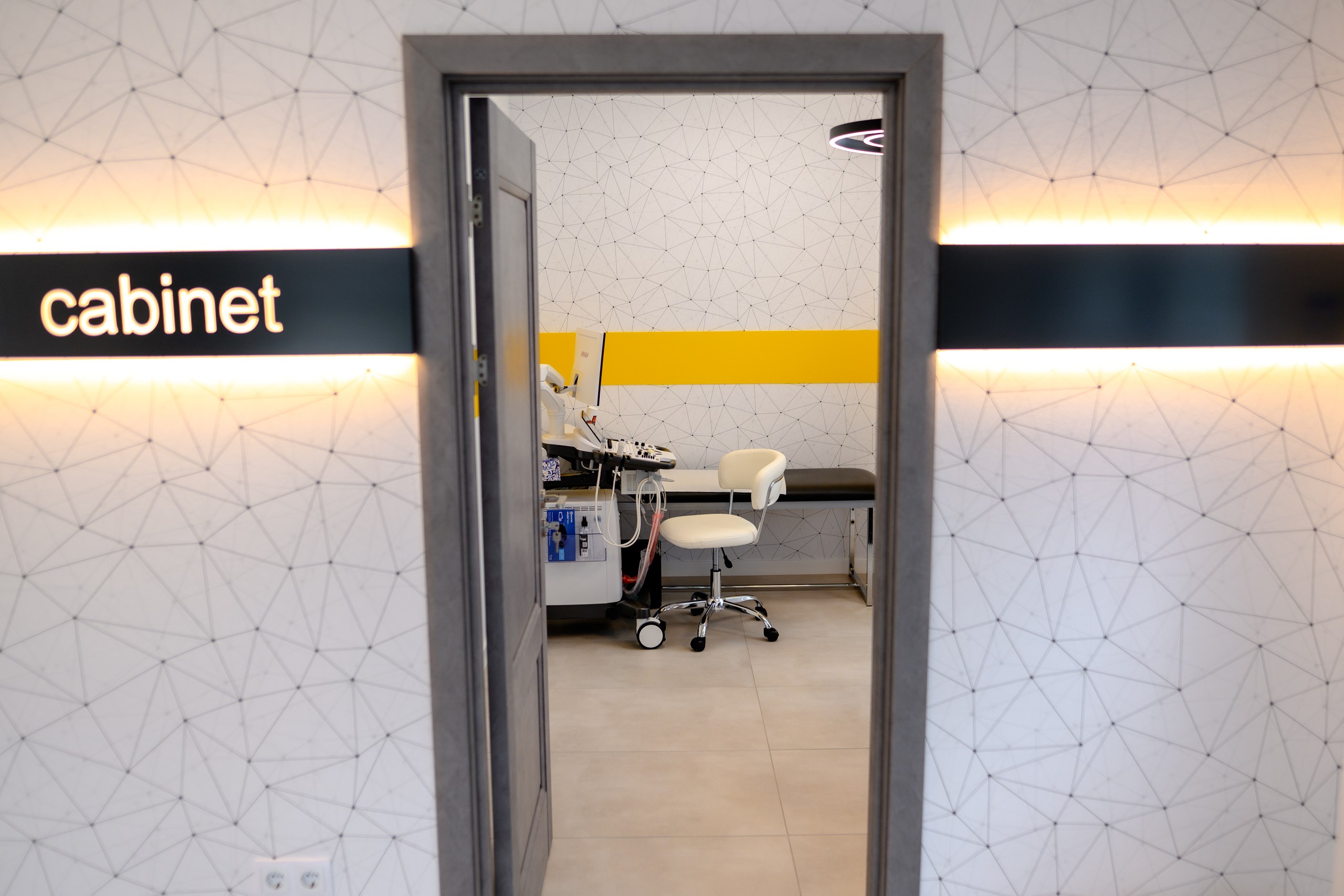 Vedere către un cabinet medical din clinica Medical Cardio Help, prin ușă deschisă și semnalizare iluminată